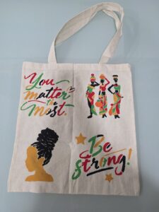 ACAP Made cream tote bag stencilled with "You matter the most", "Be strong!", three women carrying pots and a woman with an updo, in red, green, gold and black